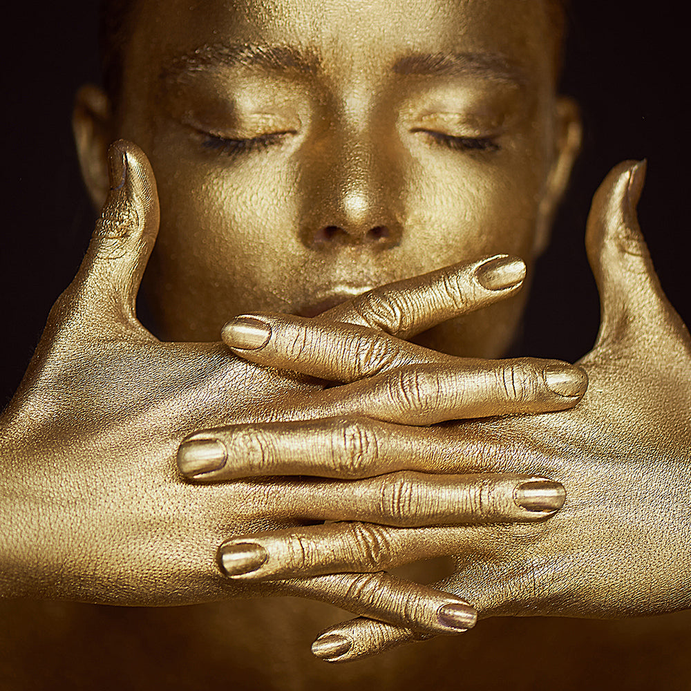 Woman covered in gold with eyes closed linking fingers together
